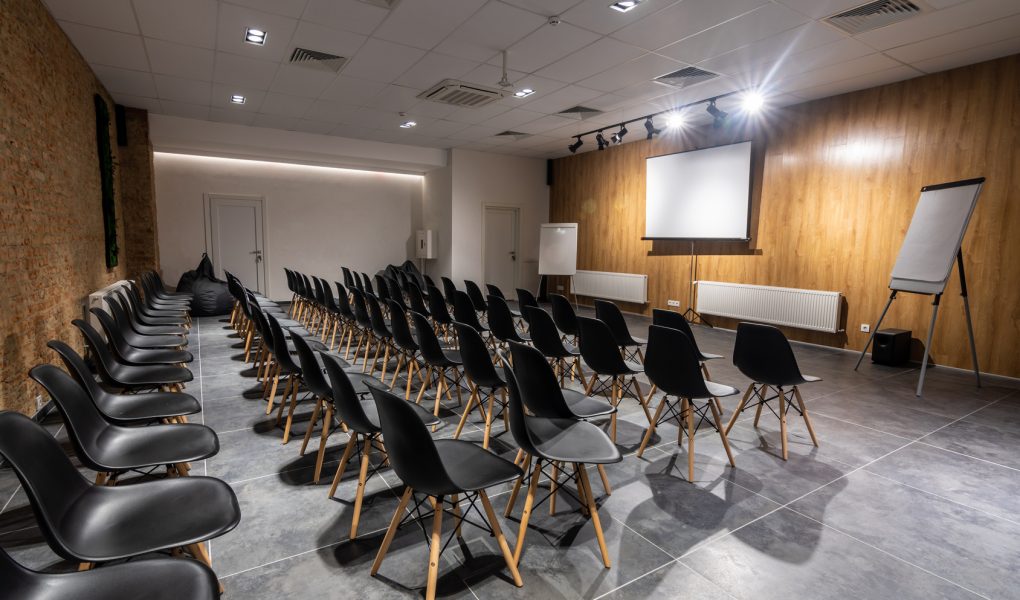Salle de séminaire vide avec chaises noires, paperboards et écran blanc