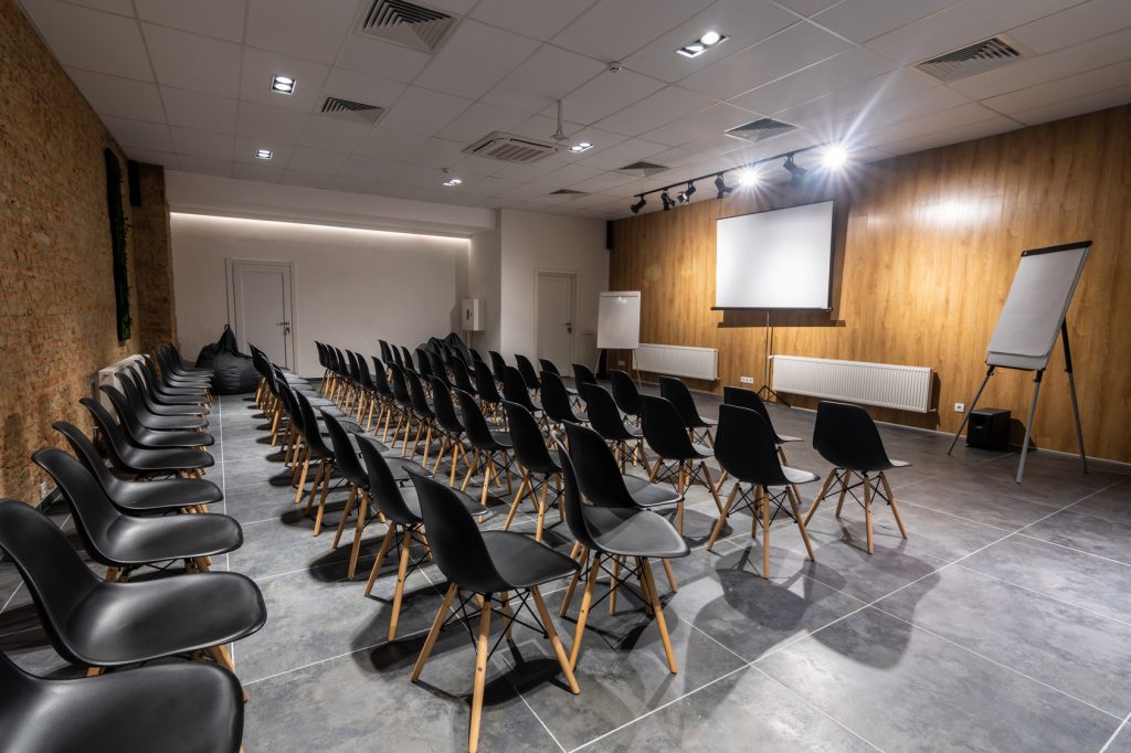 Salle de séminaire vide avec chaises noires, paperboards et écran blanc