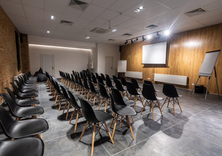 Salle de séminaire vide avec chaises noires, paperboards et écran blanc